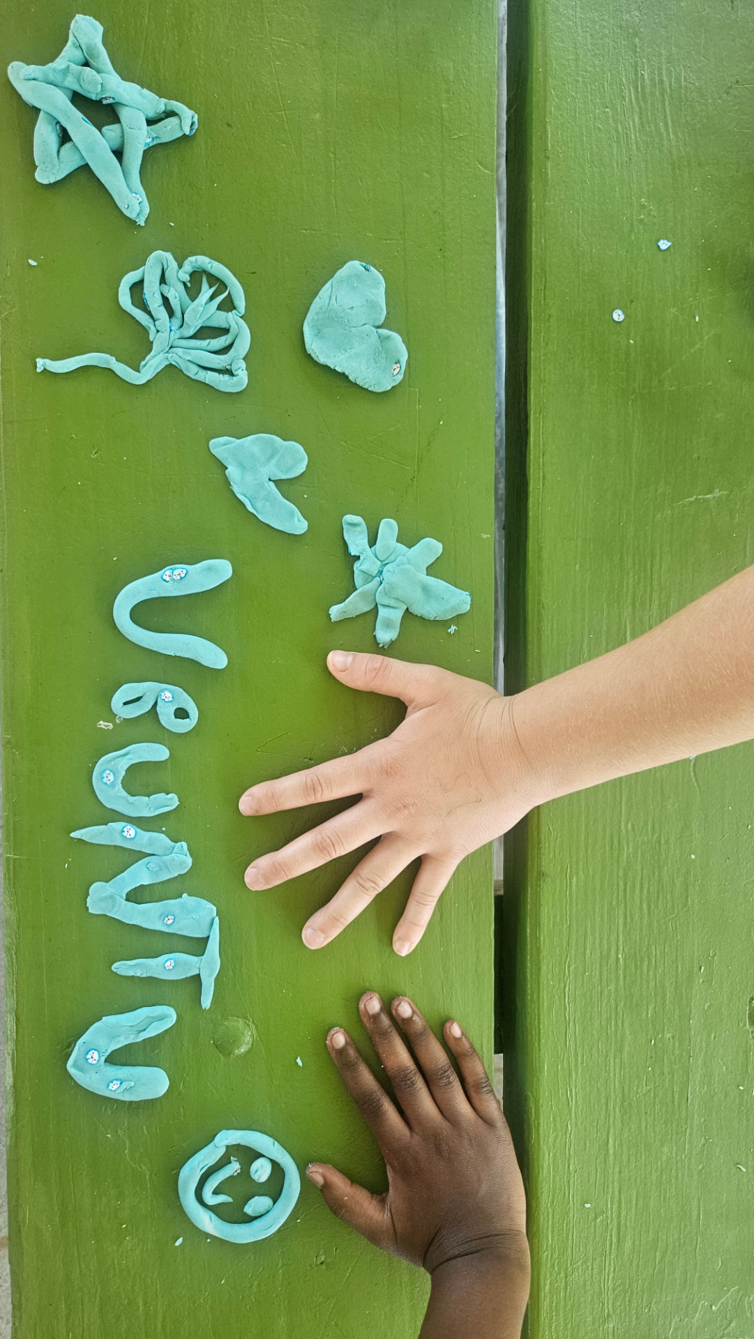 Two children's hands, one light and one dark, reaching towards the word UBUNTU shaped in modelling clay on a green wall